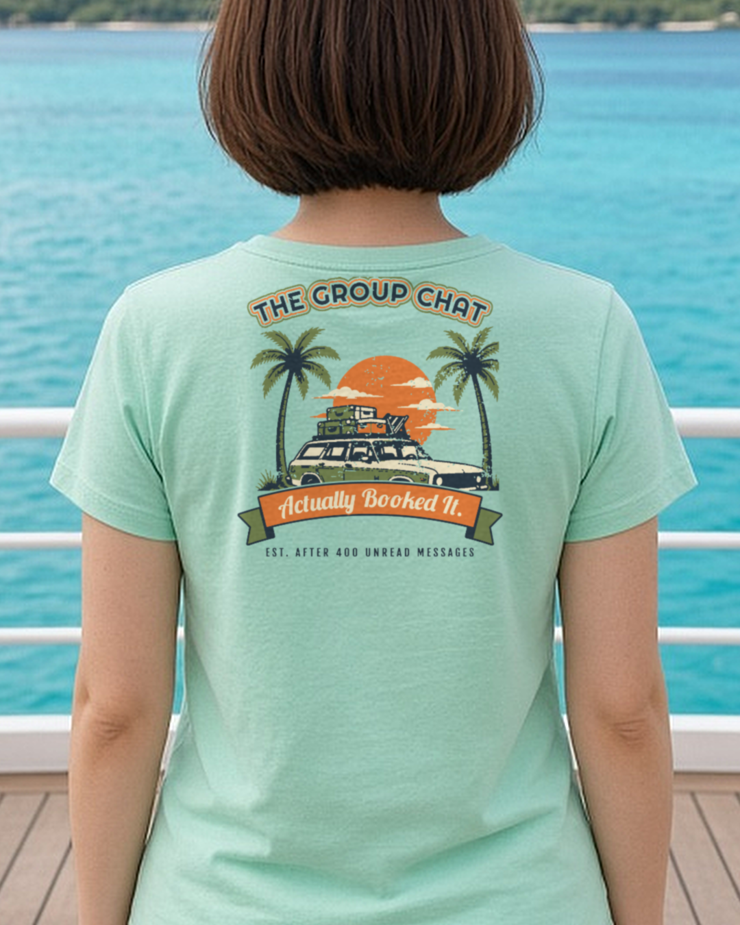Mockup: mint The Group Chat Actually Booked It tee, back print, worn at a ship rail over turquoise water